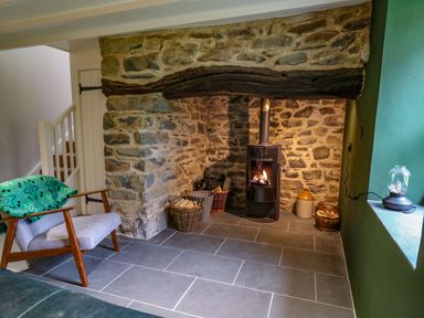 A room with a stone fireplace wood burning stove and a chair with a green blanket at Pen y Mynydd in Newport Pembrokeshire
