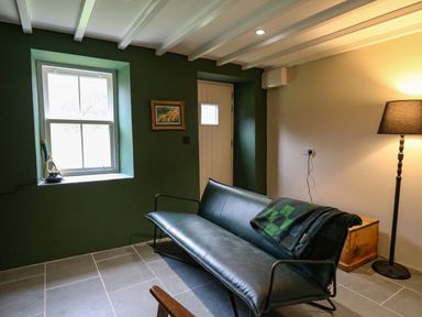 A sitting room with a green sofa a floor lamp and a window at Pen y Mynydd in Newport Pembrokeshire