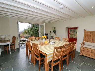 A dining room with a large table covered with a striped tablecloth surrounded by wooden chairs and an open door to a garden at Pen y Mynydd Newport Pembrokeshire