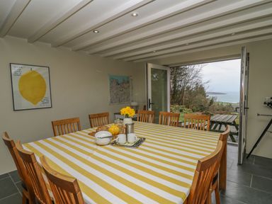 A dining room with a large table covered by a yellow and white striped tablecloth and wooden chairs at Pen y Mynydd in Newport Pembrokeshire