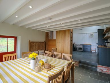 A dining room with a striped tablecloth and wooden chairs next to a kitchen with dark cabinets at Pen y Mynydd in Newport Pembrokeshire