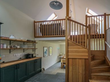 A kitchen area with open shelves and countertop next to a wooden staircase leading to a loft seating area at Pen y Mynydd in Newport Pembrokeshire