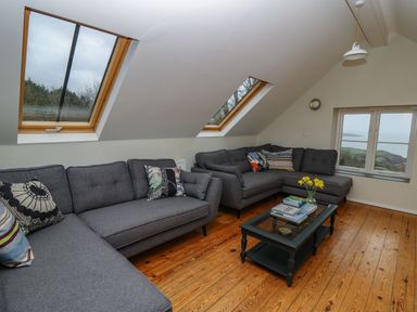 A living room with gray sofas pillows a coffee table with books and flowers skylight windows and a window with a view at Pen y Mynydd in Newport Pembrokeshire