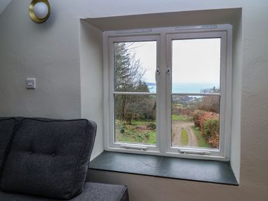 A window with a view of a dirt path and the sea beyond next to a gray upholstered chair at Pen y Mynydd in Newport Pembrokeshire