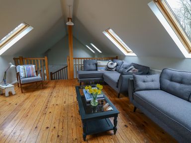 An attic living room with gray sofas a wooden chair a black glass coffee table with flowers and books wooden floors and skylight windows at Pen y Mynydd in Newport Pembrokeshire