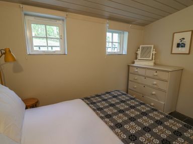 A bedroom with a bed a side table a lamp two windows a dresser with a mirror and a picture on the wall at Pen y Mynydd in Newport Pembrokeshire