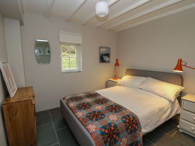 A bedroom with a double bed bedside tables with orange lamps a wooden chest of drawers and a window at Pen y Mynydd in Newport Pembrokeshire