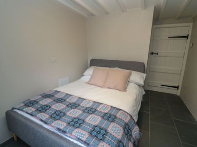 A small bedroom with a grey bed frame a white bedspread two beige pillows a patterned blanket on a tiled floor at Pen y Mynydd in Newport Pembrokeshire