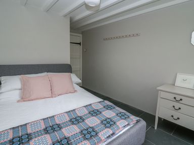 A bedroom with a gray upholstered bed with pink pillows and a patterned blanket next to a white dresser with a framed picture at Pen y Mynydd Newport Pembrokeshire