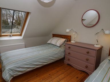 A bedroom with two single beds a chest of drawers with two lamps and a round mirror at Pen y Mynydd in Newport Pembrokeshire