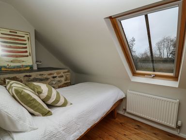 A bedroom with a white bed and striped pillows under a slanted ceiling with a skylight window at Pen y Mynydd in Newport Pembrokeshire