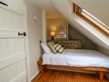 A bedroom with a single bed with white bedding and striped pillows under a skylight at Pen y Mynydd in Newport Pembrokeshire