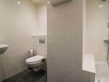 A bathroom with a wall-mounted toilet, toilet paper holder, small sink, and part of a bathtub with a shower at Pen y Mynydd in Newport Pembrokeshire