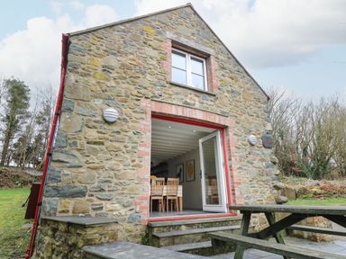 Stone house with open door showing dining table and chairs next to wooden picnic bench outdoors at Pen y Mynydd in Newport Pembrokeshire