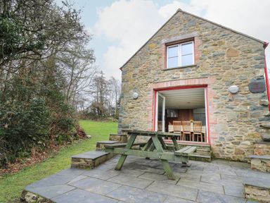 An outdoor patio with a wooden picnic table and a stone building with open doors showing a dining table at Pen y Mynydd in Newport Pembrokeshire