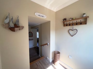 A hallway with wall decor including wooden sailboats and a heart hanging on a coat rack at May Bell Cottage in Dersingham