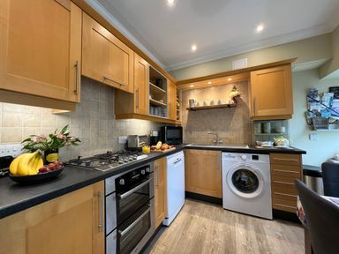 A kitchen with wooden cabinets a gas stove dishwasher washing machine and countertop items at May Bell Cottage in Dersingham