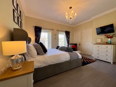A bedroom with a bed bedside table lamp dresser TV and two windows at May Bell Cottage in Dersingham