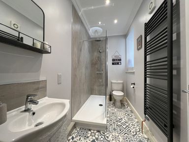 A bathroom with a sink and mirror on the left a walk-in shower in the center a toilet on the right and a black towel radiator at May Bell Cottage in Dersingham