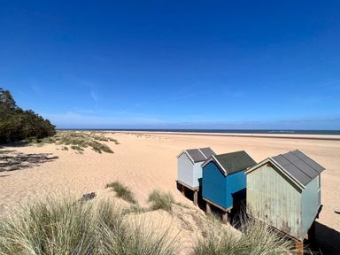 Beach huts on a sandy beach with dunes and sea in the background at May Bell Cottage in Dersingham