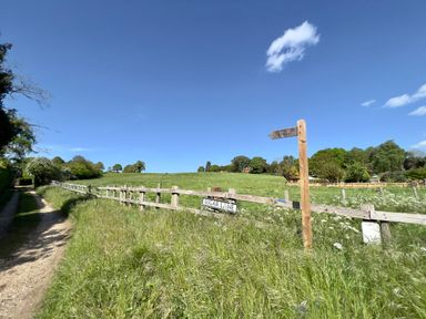 A dirt path next to a wooden fence with signs for Sugar Lane and restricted byway in a rural area at May Bell Cottage in Dersingham