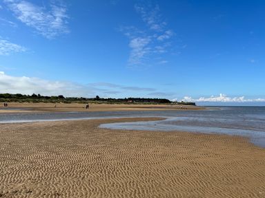 A sandy beach with ripples in the sand and a few people walking near the water at May Bell Cottage in Dersingham