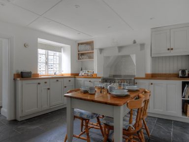 A kitchen with a wooden table set for four and white cabinets with wooden countertops at 12 Mill Green in Lyme Regis