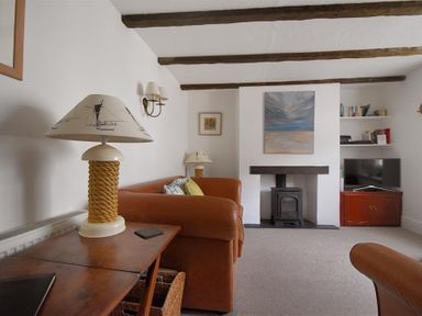 A living room with brown leather sofas wooden table lamps a wood burning stove and a TV on a cabinet at 12 Mill Green in Lyme Regis