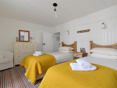 A bedroom with two single beds with yellow blankets and white towels a chest of drawers and a white armchair at 12 Mill Green in Lyme Regis