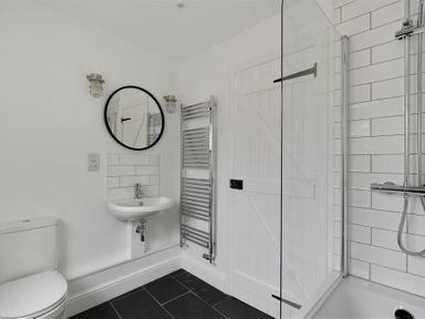 A bathroom with a toilet sink round mirror heated towel rail and a shower area at 12 Mill Green in Lyme Regis