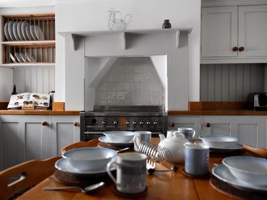 A kitchen with a dining table set with bowls mugs and a teapot and a stove with cabinets in 12 Mill Green Lyme Regis
