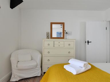 A bedroom with a white armchair a cream dresser with a mirror and a bed with white towels on a yellow blanket at 12 Mill Green in Lyme Regis