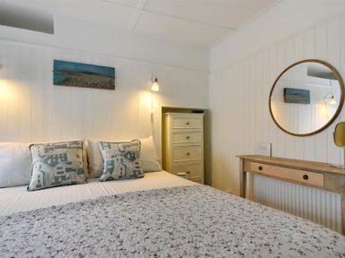 A bedroom with a bed with pillows and a quilt a wooden dresser and a wooden table with a round mirror at 12 Mill Green in Lyme Regis