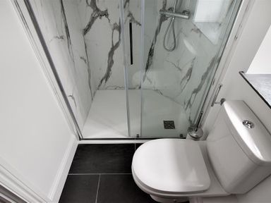 A bathroom with a white toilet and a glass shower enclosure with marble-patterned walls at 12 Mill Green in Lyme Regis