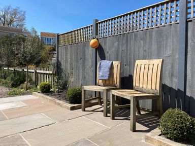 Two wooden chairs on a stone patio next to a wooden fence with plants and bushes nearby at 12 Mill Green in Lyme Regis