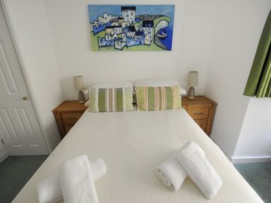 A bedroom with a double bed two wooden bedside tables lamps pillows rolled towels and a painting above the bed at Sea Fever Lyme Regis