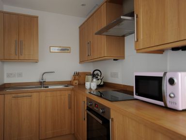 A kitchen with wooden cabinets a sink a stovetop an oven a pink microwave and kitchen utensils on the counter at Sea Fever in Lyme Regis