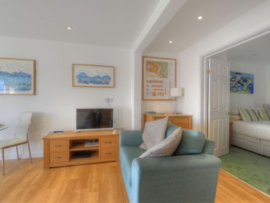 A living room with a blue armchair a wooden TV stand with a television and framed artwork on the walls at Sea Fever in Lyme Regis