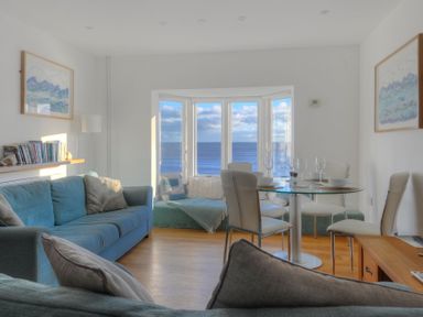A living room with blue sofas a glass dining table and a bay window with sea view at Sea Fever Lyme Regis