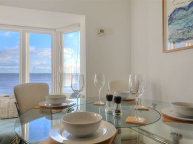 A dining area with a glass table set with bowls plates wine glasses and salt and pepper shakers beside large windows overlooking the sea at Sea Fever in Lyme Regis