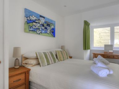 A bedroom with a double bed striped pillows wooden bedside tables lamps a wooden desk green curtains and a window at Sea Fever Lyme Regis