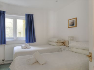 A bedroom with two single beds white linens rolled towels blue curtains and a nightstand with a lamp at Sea Fever Lyme Regis