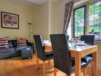 A dining area with a wooden table and four black chairs next to a window and a black leather sofa with cushions at Coram Lodge in Lyme Regis