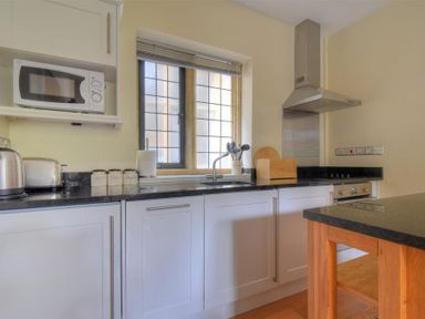 A kitchen with white cabinets a microwave toaster kettle utensils on the counter and a window at Coram Lodge Lyme Regis