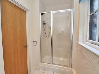 A bathroom with a glass shower enclosure a wooden door and a frosted window at Coram Lodge in Lyme Regis