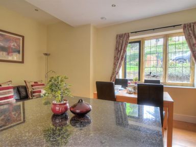 A dining area with a wooden table and black chairs near a window and a corner sofa with striped cushions at Coram Lodge in Lyme Regis