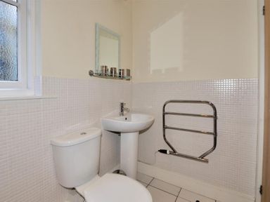 A bathroom with a toilet, sink, heated towel rail, mirror, and frosted window at Coram Lodge in Lyme Regis