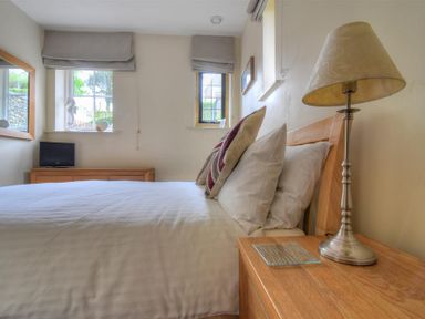 A bedroom with a bed pillows a bedside table with a lamp a dresser with a small television and two windows at Coram Lodge in Lyme Regis