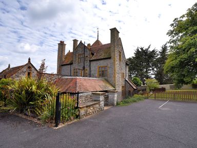 An old stone house with multiple chimneys surrounded by a garden and trees at Coram Lodge in Lyme Regis