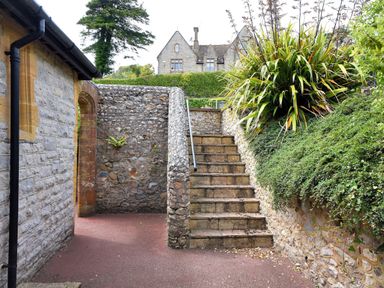 Stone stairs with metal railing next to a stone wall and plants with a building in the background at Coram Lodge in Lyme Regis